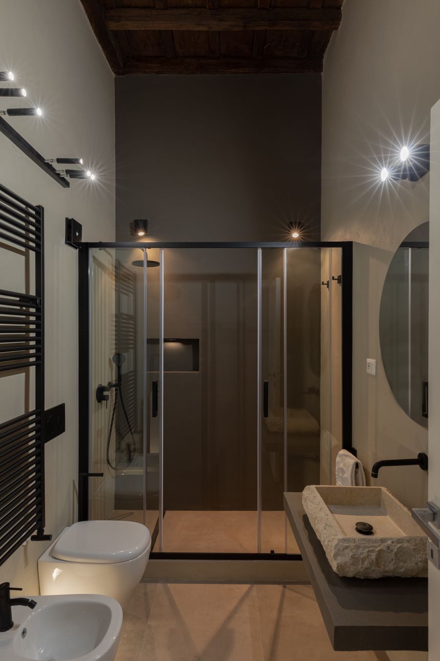 Bagno con doccia in vetro, travi a vista e luci puntiformi