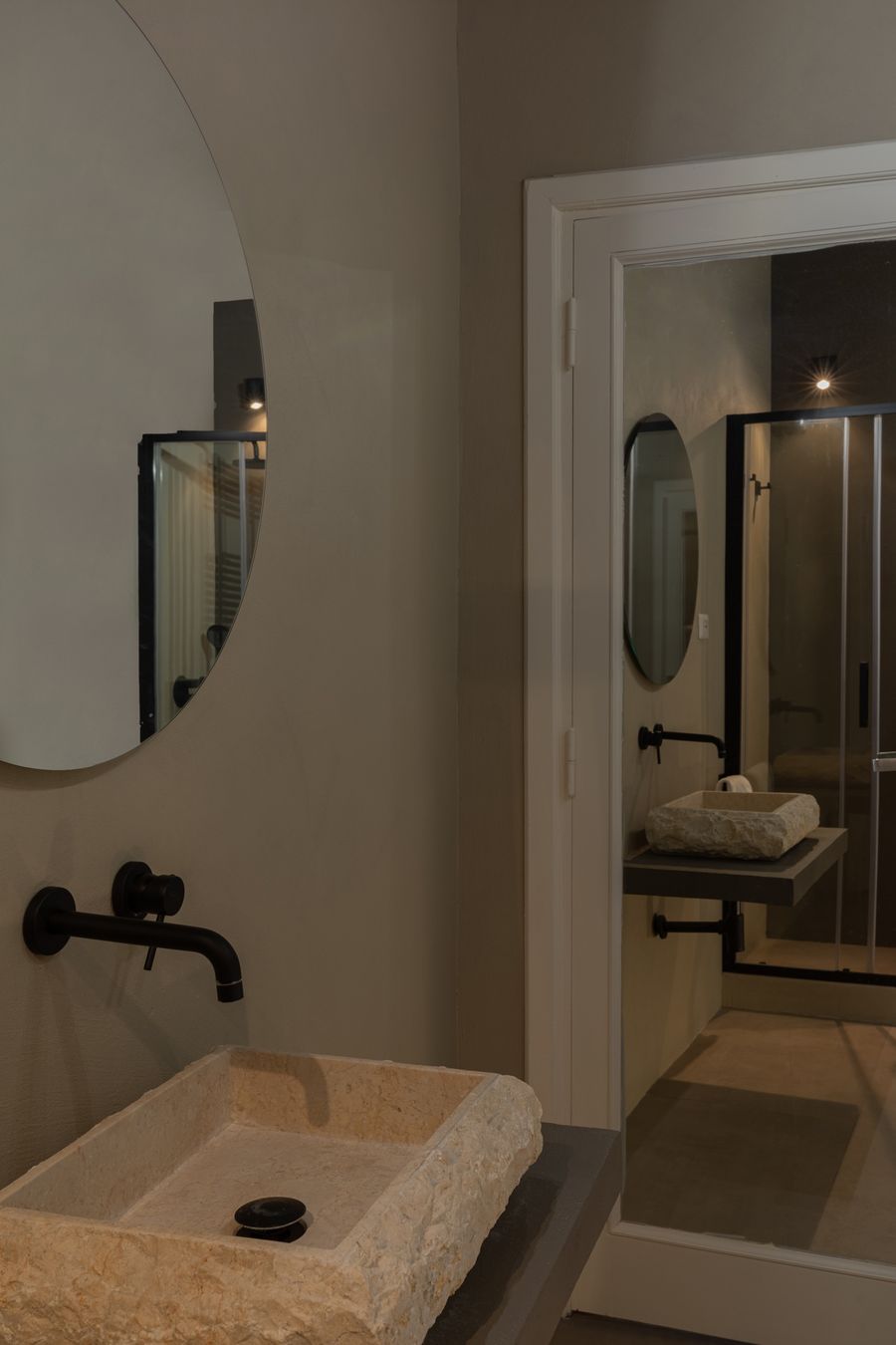 Lavabo in pietra grezza con rubinetteria nera e specchio tondo